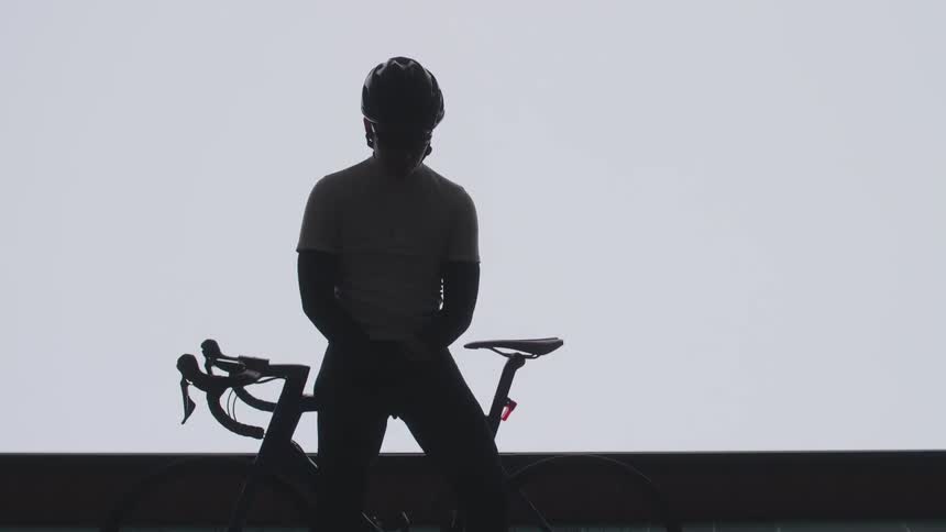 A bicyclist poses with his bicycle in front of a brightly lit screen