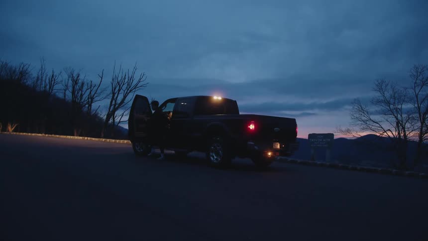 A man gets out of his truck next to a sign near the road