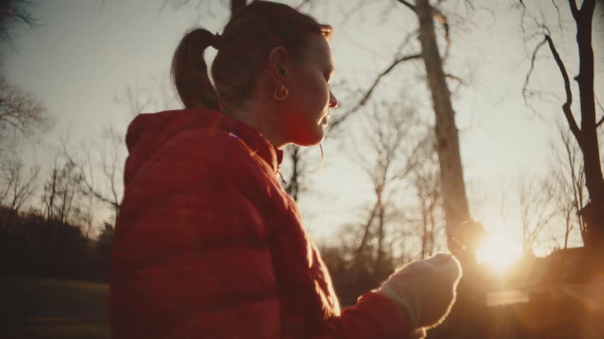 Woman in a red jacket holding a dry white rose against a sun in the background