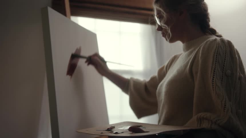 A woman begins painting on a blank canvas inside of a room