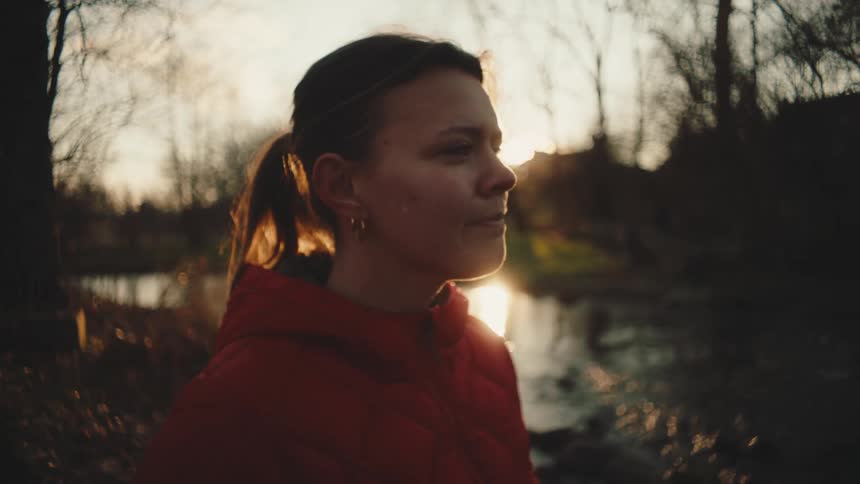 A woman sighs and walks away from the bank of a stream