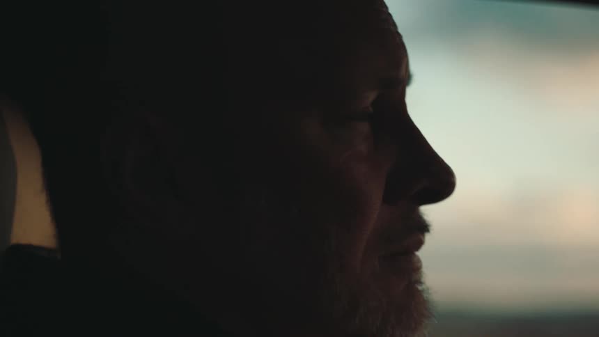 An older man cries while riding in a car