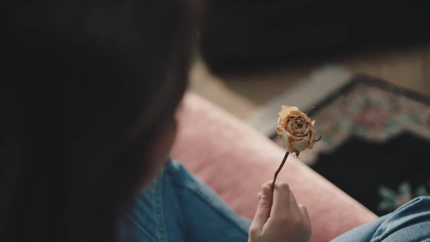 A woman is sitting at home holding a single flower