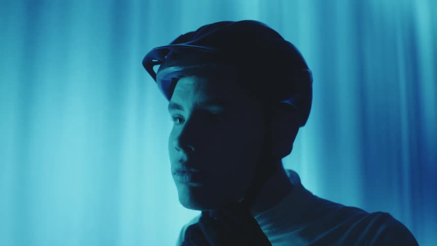 Portrait of a man in a cyclist putting on a protective helmet indoors with a blue light in the background