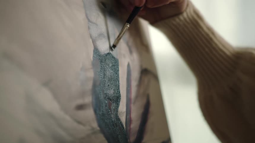 Closeup of a hand holding a brush and painting a picture