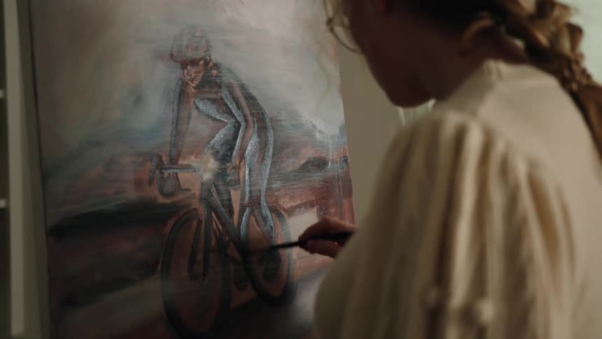 A young woman with glasses paints a picture of a woman riding a bicycle
