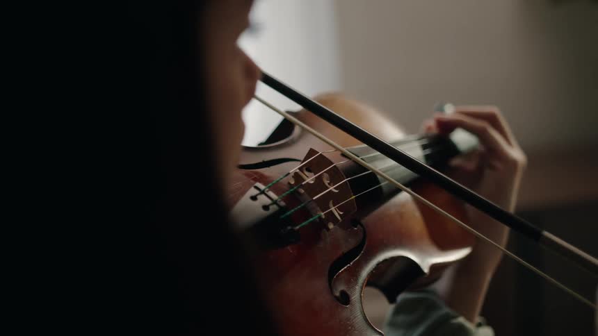 An asian woman gently plays a violin in a living room
