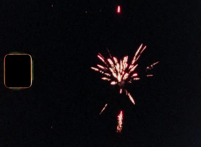 Night sky with red fireworks flying up into the darkness and exploding with bright light and sparkles during a nighttime celebration on Super 8 film