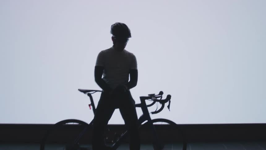 Silhouette of a cyclist with a helmet and bicycle against a white screen in the background
