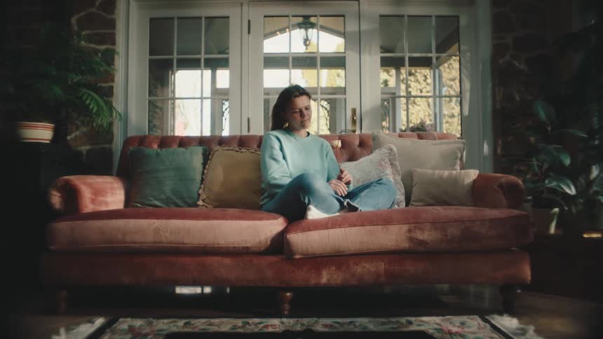 Woman sitting on a sofa holding a white flower and looking at it thoughtfully