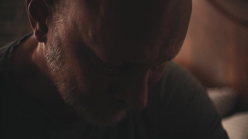 Close up of the face of a balding middleaged man in a dimly lit room