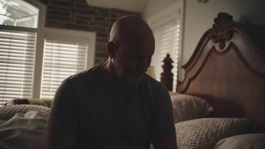 Man sitting on a bed with sad facial expression