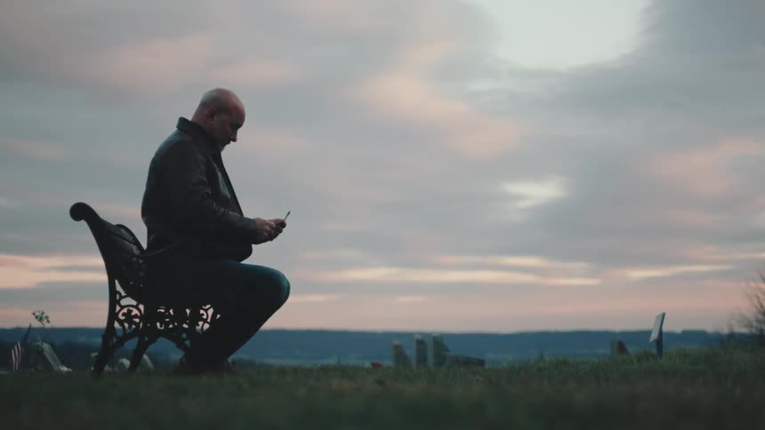 Lone man sitting on a bench in a garden with a cloudy sky in red tones