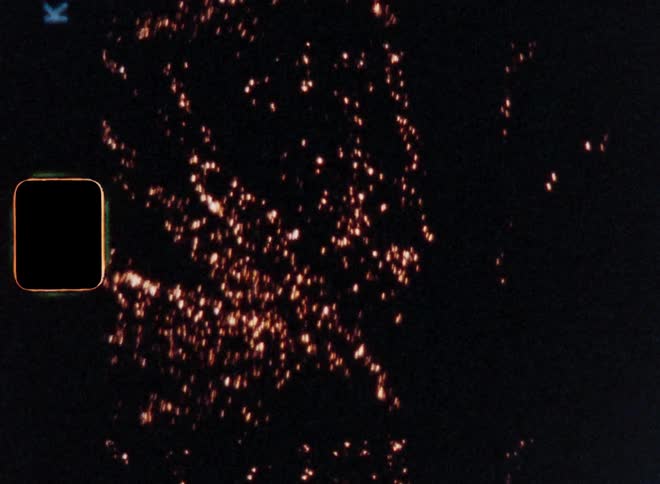 Super 8 film footage following an aerial firework rocket flying into the dark night sky before it explodes with bright light and sparkles illuminating the streets on New Year’s Eve