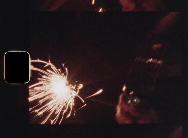 Sparklers superimposed over two people clinking glasses while toasting and a woman drinking the champagne while smiling at her partner or friend in the dark night on the streets illuminated by the sparkling fireworks