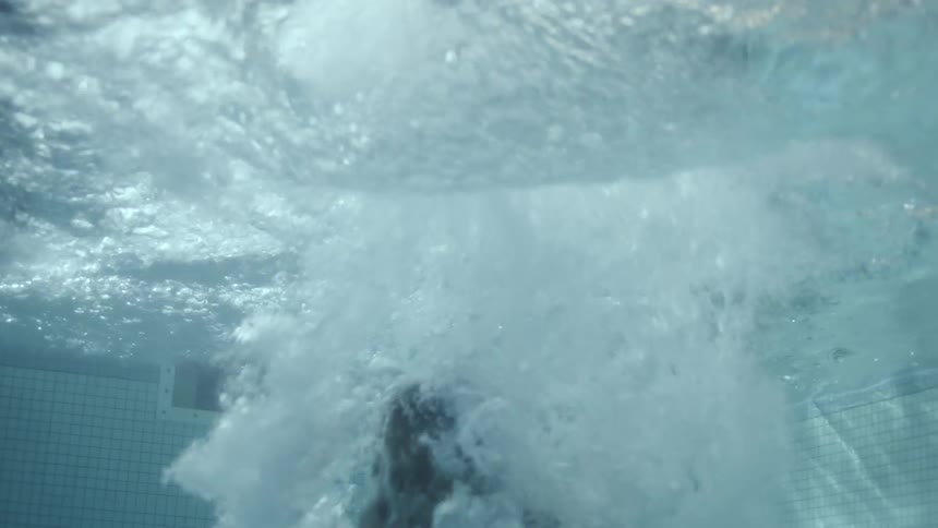 Underwater footage of a boy jumping into a pool surrounded by bubbles