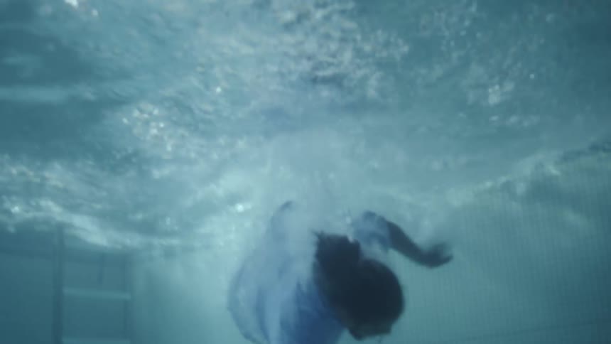 Underwater footage of a fully clothed man falling into a pool to retrieve something