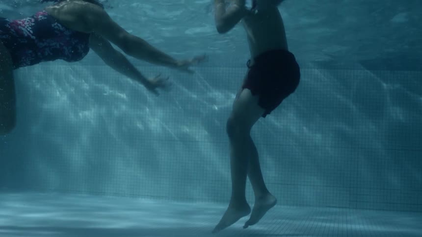 A woman and a child duck under the water in a pool