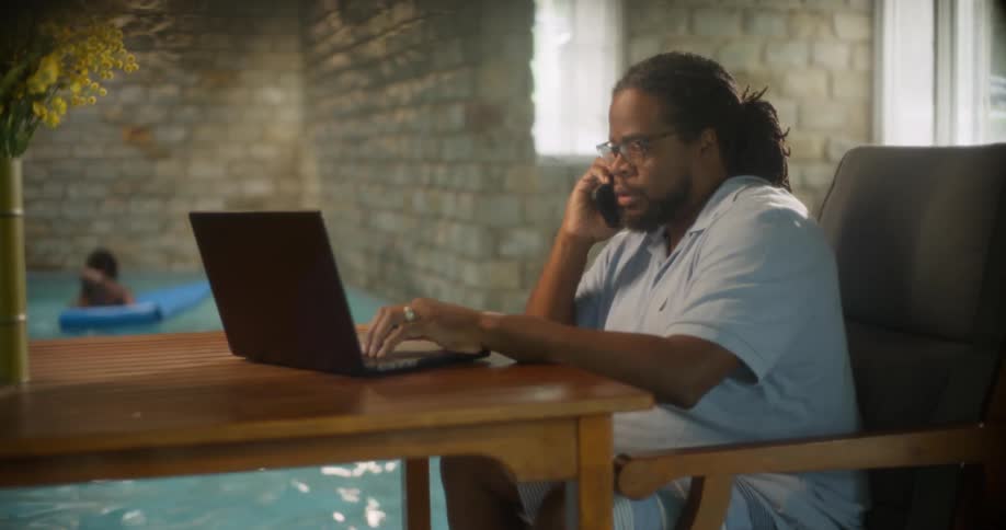 A man working on a laptop sitting on a desk next to an indoors swimming pool