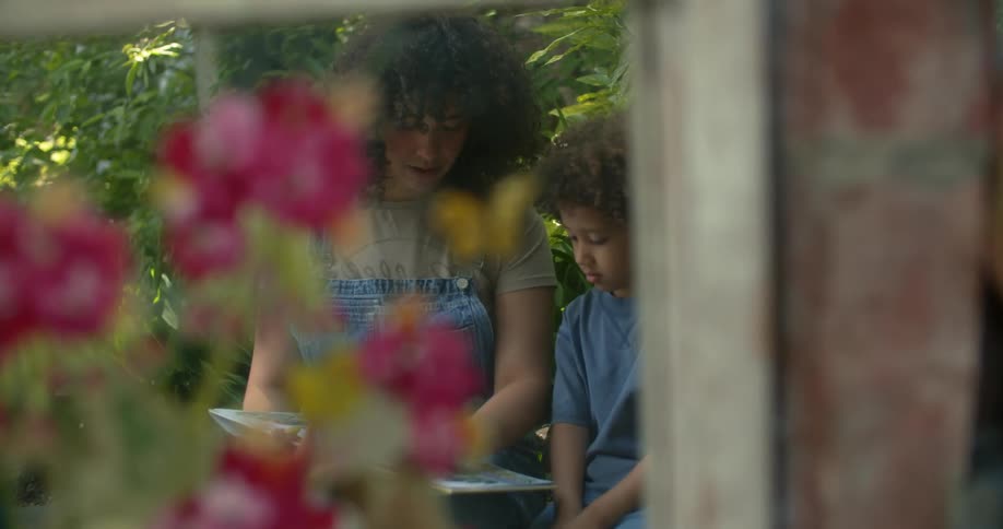 Mother reading a storybook to her son while they are sitting in a garden