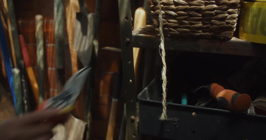 A closeup of a hand picking up gardening shears from a shed