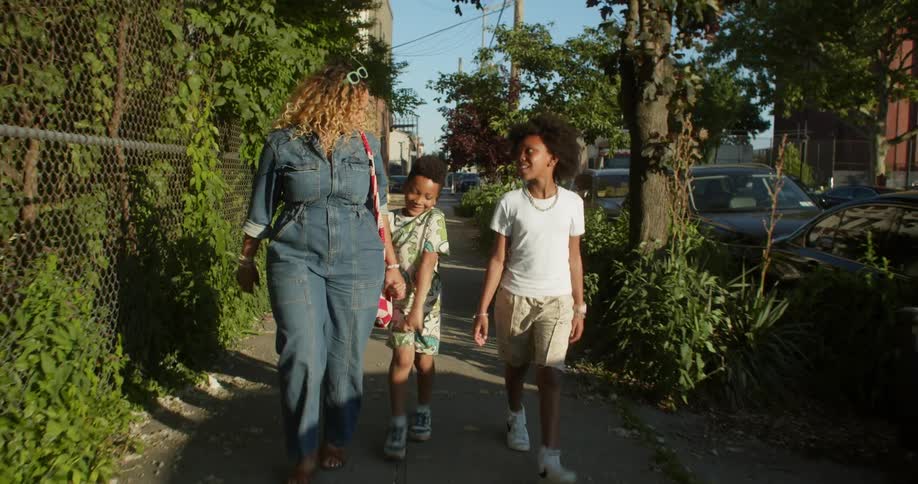 Woman walking with two small children on the sidewalk of a street