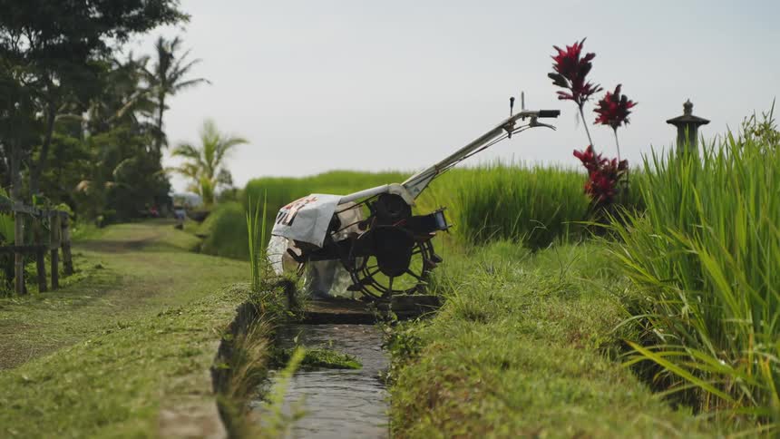 A farming machine rests over a narrow irrigation channel in a lush green field