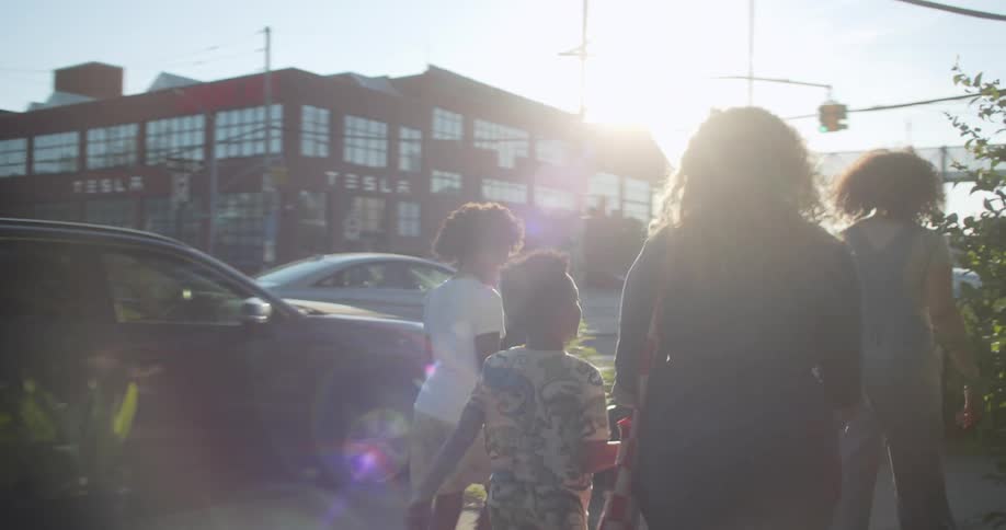 A family exits a community garden in the city walking down the sidewalk on the street
