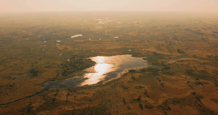 Lake surrounded by grassland reflects the sunlight on a hazy day
