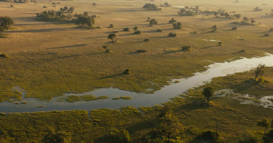 River flowing though grassland passesmultiple groves on a hazy day
