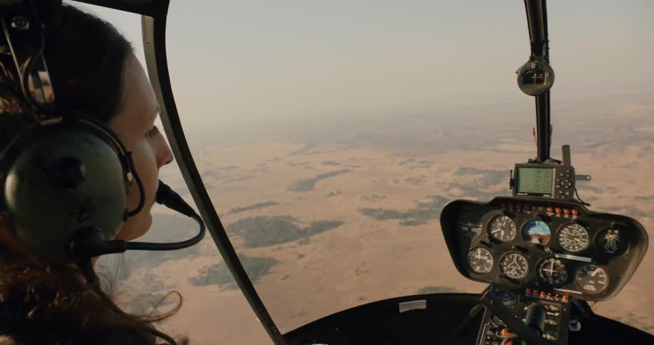 A female pilots a helicopter over a large plain