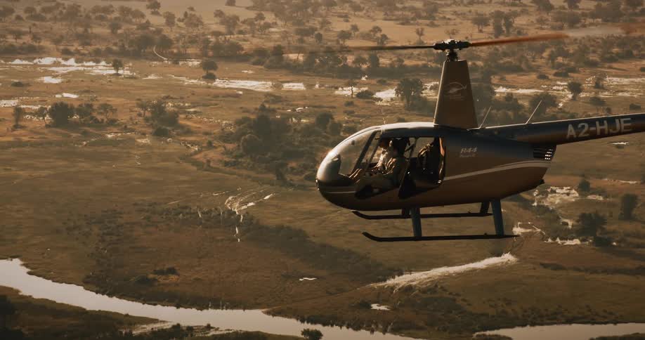A helicopter with two people in it flies over a swampy area