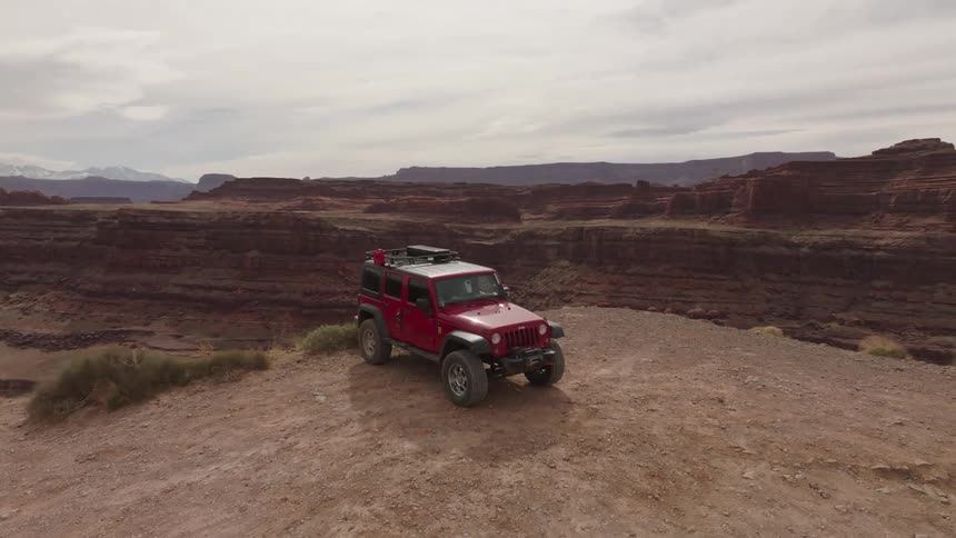 A red offroad car parked next to a cliff in a region with canyons