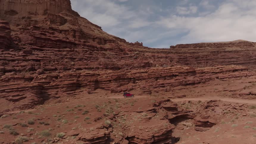 Red sports jeep traveling through a natural environment surrounded by canyons