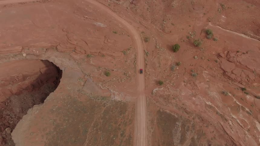 An aerial view of a truck driving down dirt road winding through a rugged arid landscape