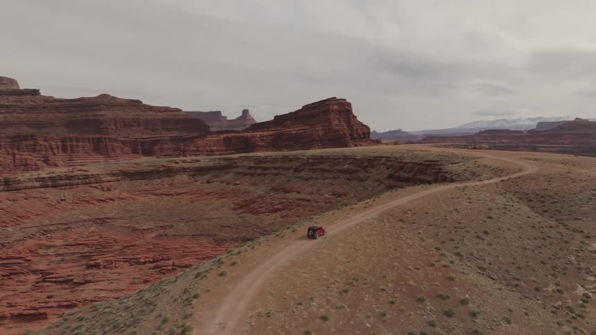 A car drives down a dirt road winding through a desert landscape with rock formations