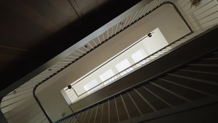 A view of a staircase with a dark handrail looking up at a skylight