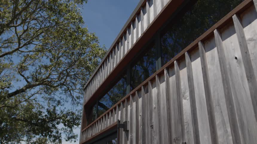 A modern building with a wooden facade and large glass windows stands against a clear blue sky