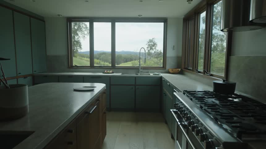 A modern kitchen interior with a view of the outdoors through large windows featuring stainless steel appliances wooden countertops
