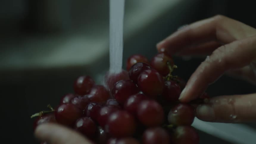 Pair of hands holding a bunch of grapes and washing in the sink