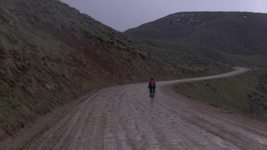 Cyclist riding up a narrow inclined dirt road through the hills