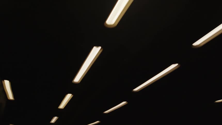 Cars driving on highway through a dark tunnel with fluorescent ceiling lights