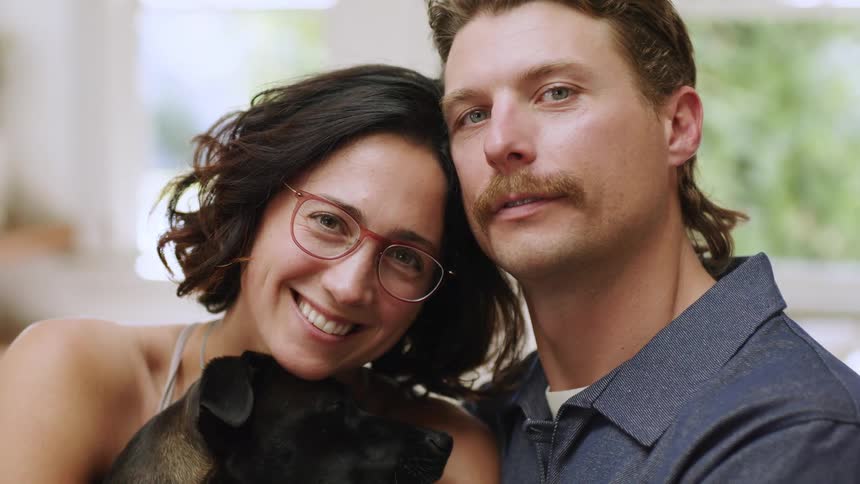 A young couple holding a small black dog smile for the camera
