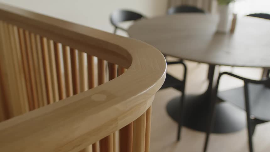 Closeup on a wooden handrail inside a house and in the background a small table in a living room