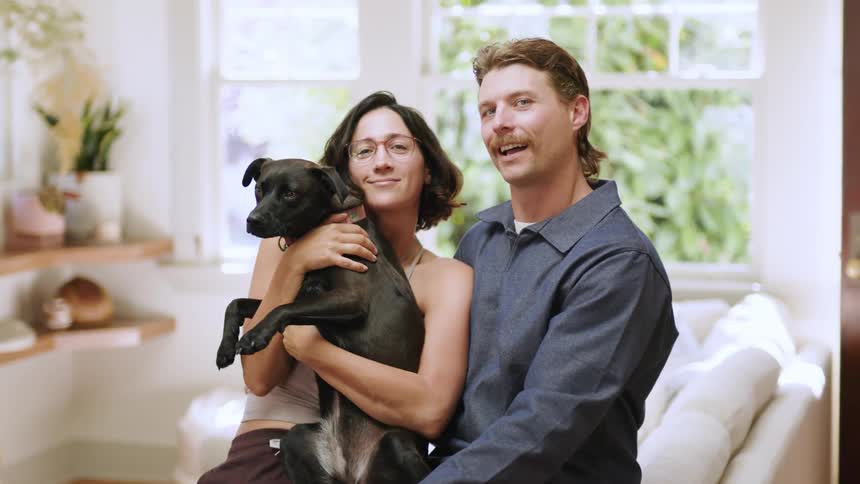 Smiling couple sitting in the living room with a woman holding a dog