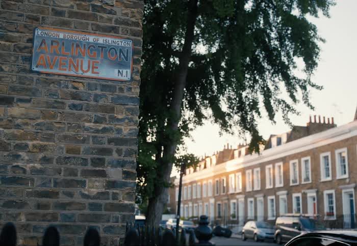 A street sign for arlington avenue n1 on a brick wall with houses and cars parked in warm sunlight