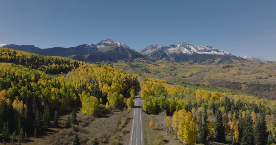 Aerial panorama of a stretch of highway surrounded by conifers and mountains on the horizon