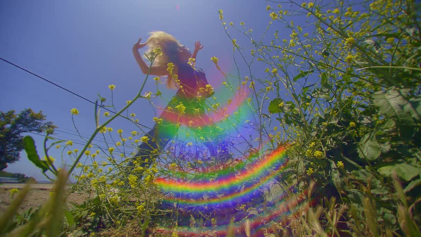 Blonde woman dancing next to a bed of green and yellow flowers and moving her hair
