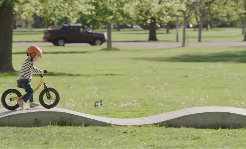 A little boy is on top of a yellow bicycle and going along a path with some small ramps