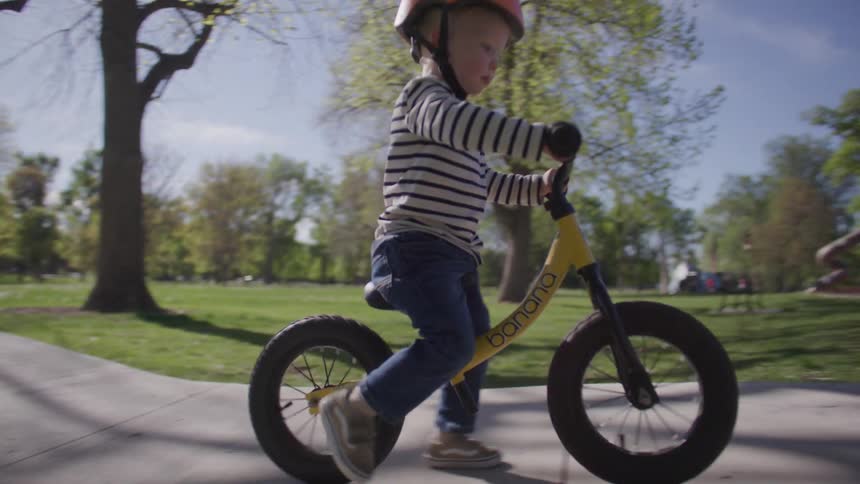 Blonde boy in a helmet learning to ride a bicycle without training wheels in a park